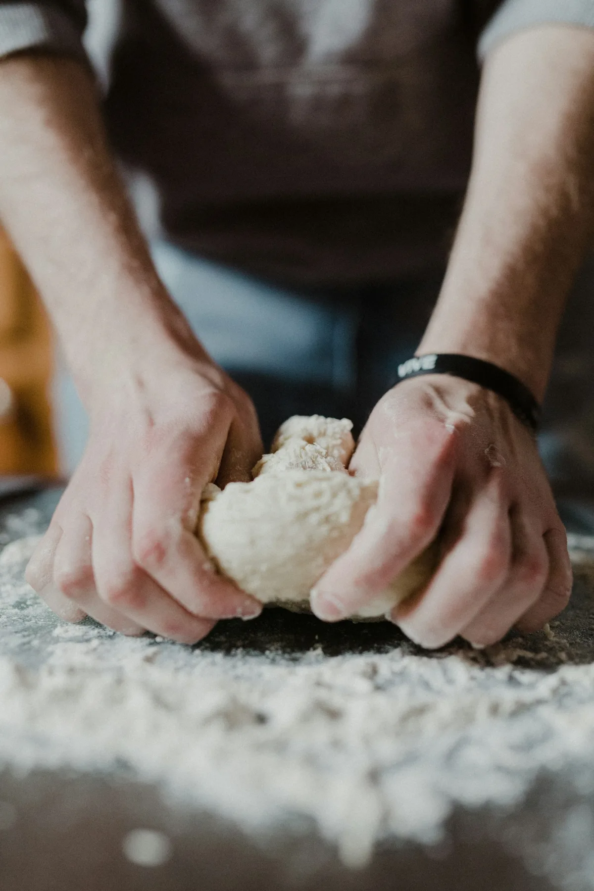 Baker's hands kneading dough on a floured bench